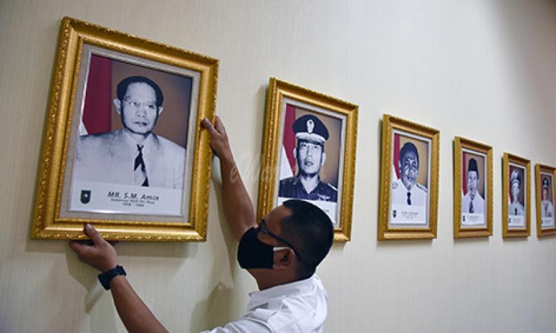Seorang pegawai merapikan letak foto Gubernur Riau pertama, Sultan Mohammad (SM) Amin Nasution, di Kantor Gubernur Riau, Kota Pekanbaru, Senin (9/11/2020). (antarafoto)