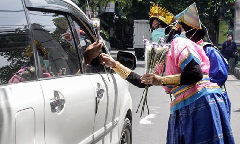 Tenaga kesehatan memakai pakaian adat saat membagikan bunga kepada pengendara di depan RS Siti Hajar Sidoarjo, Jawa Timur, Senin (21/12/2020). (antarafoto)